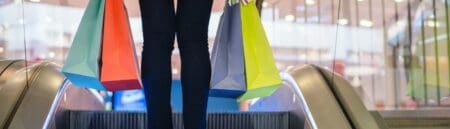 Woman on an escalator holding retail shopping bags.