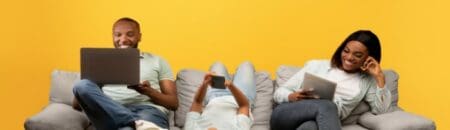 A family lying on their sofa each using different digital devices.
