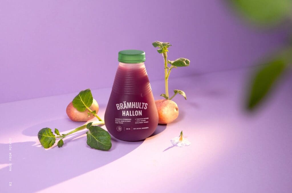 Photograph of TomorrowMachine's juice bottle, containing red fruit juice, some fruit on either side of the bottle and lilac background.